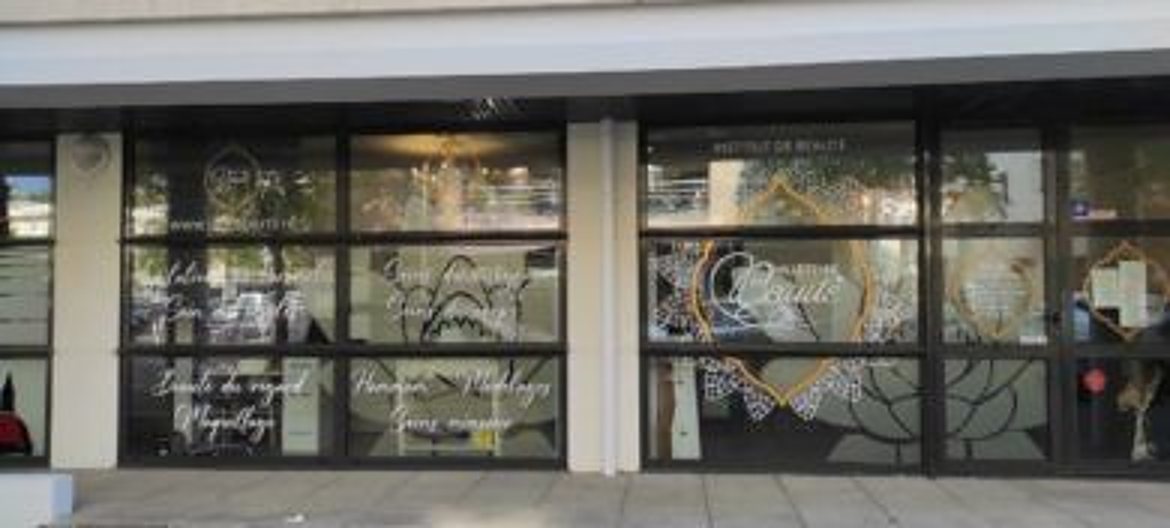 Façade vitrée d'un institut de beauté dont les vitres sont ornées de motifs décoratifs blancs et dorés ainsi que de textes sur les soins proposés.